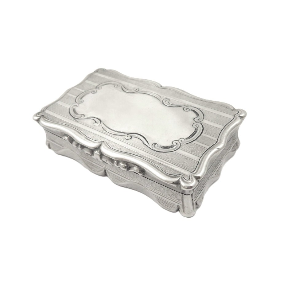 A rectangular Victorian sterling silver snuff box featuring scalloped edges, engine-turned linear engraving, and an unengraved scrollwork cartouche on the lid. View X