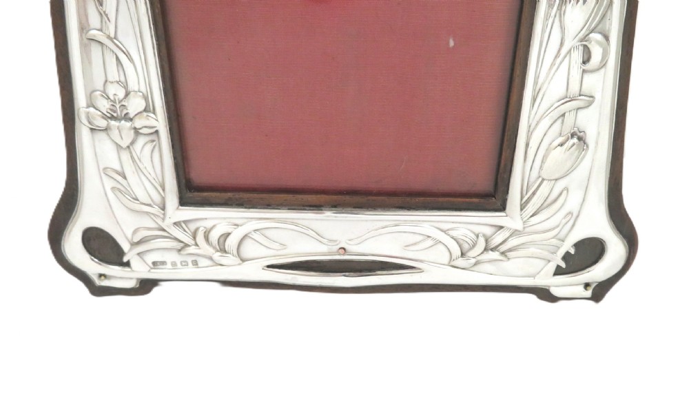 An Edwardian sterling silver Art Nouveau picture frame featuring embossed floral motifs mounted on a dark wood easel backing. View III
