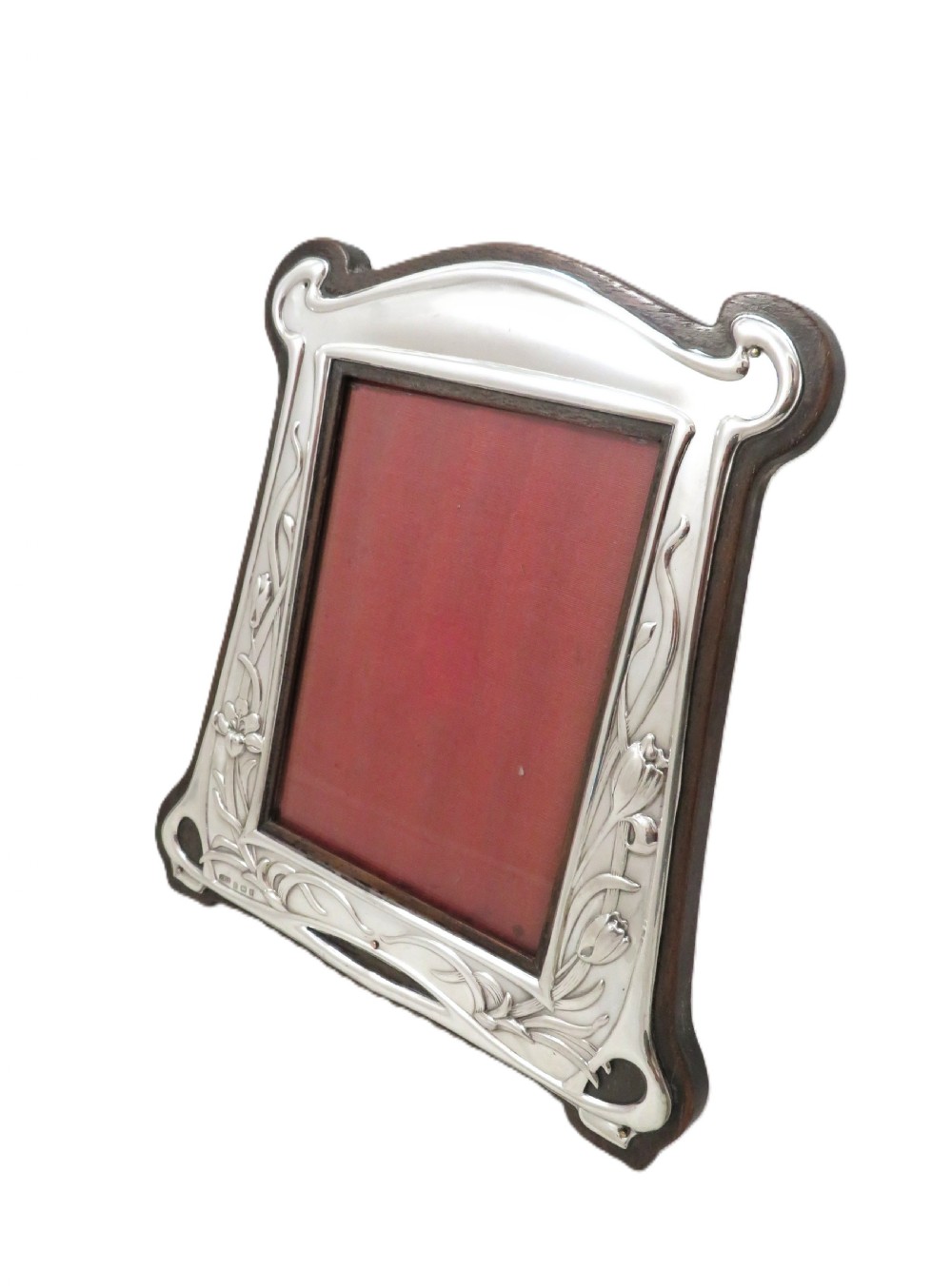 An Edwardian sterling silver Art Nouveau picture frame featuring embossed floral motifs mounted on a dark wood easel backing. View VI