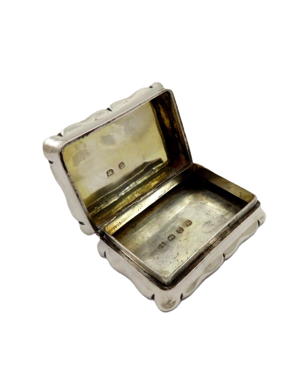 An antique Victorian rectangular sterling silver box featuring chased floral scrollwork and a central engraved crest on the lid. View III