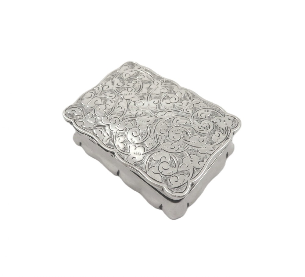 An antique Victorian rectangular sterling silver box featuring chased floral scrollwork and a central engraved crest on the lid. View IV