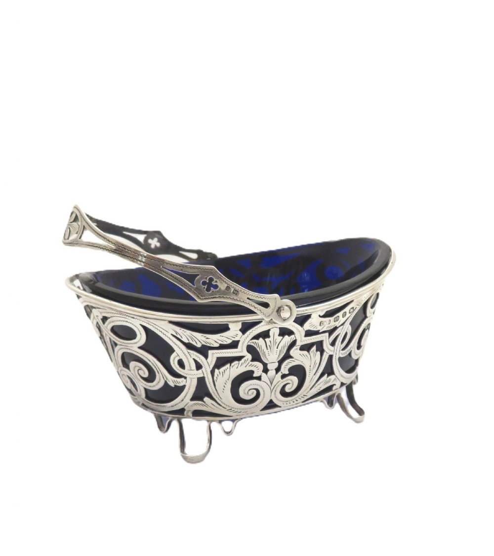 An antique Victorian sterling silver basket with intricate scrollwork piercing, an overhead swing handle, four small feet, and a dark cobalt blue glass liner. View VII