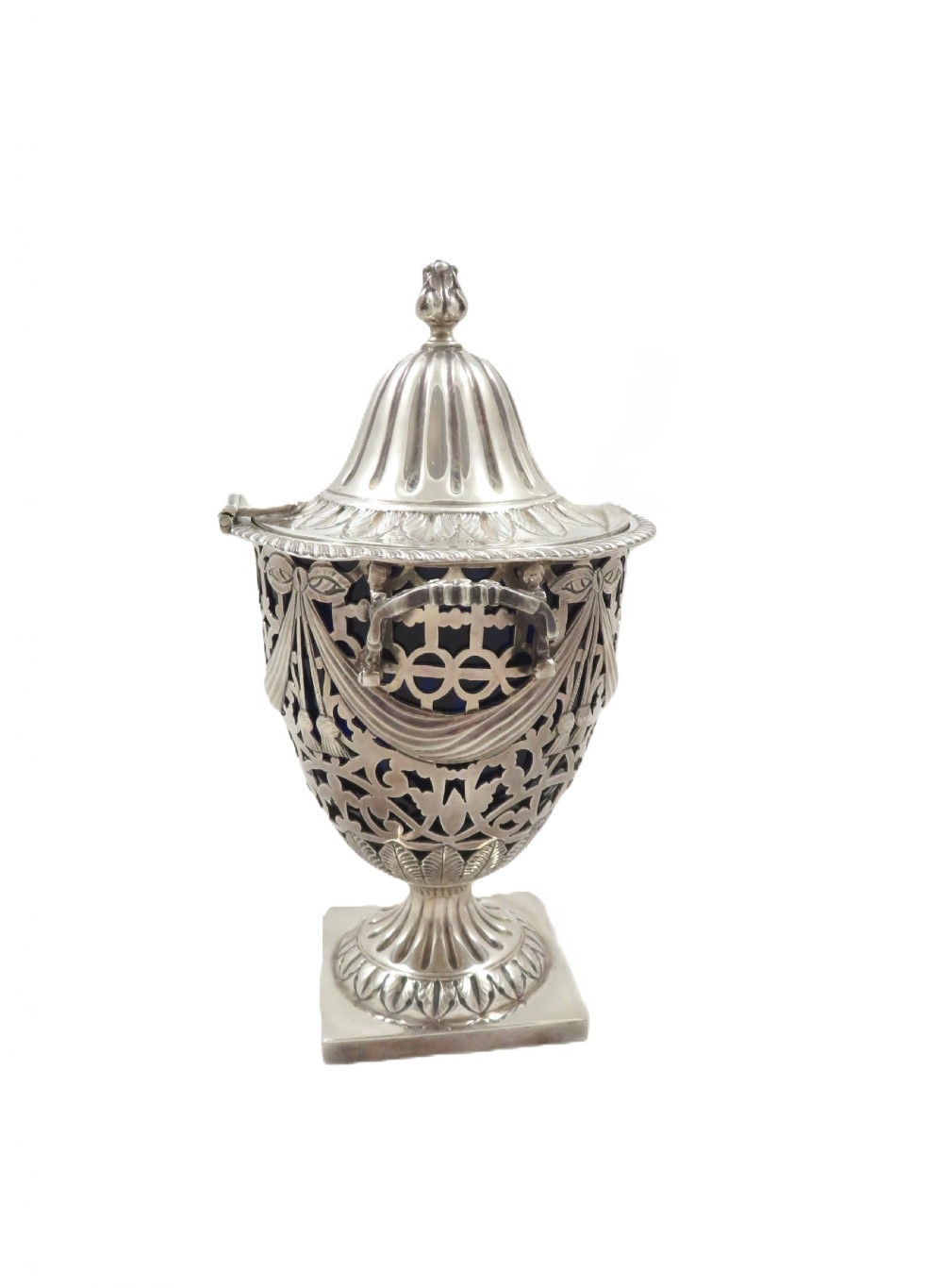 An Edwardian sterling silver sugar urn featuring pierced garland decoration, a cobalt blue glass liner, a fluted lid, and a silver spoon. View IV