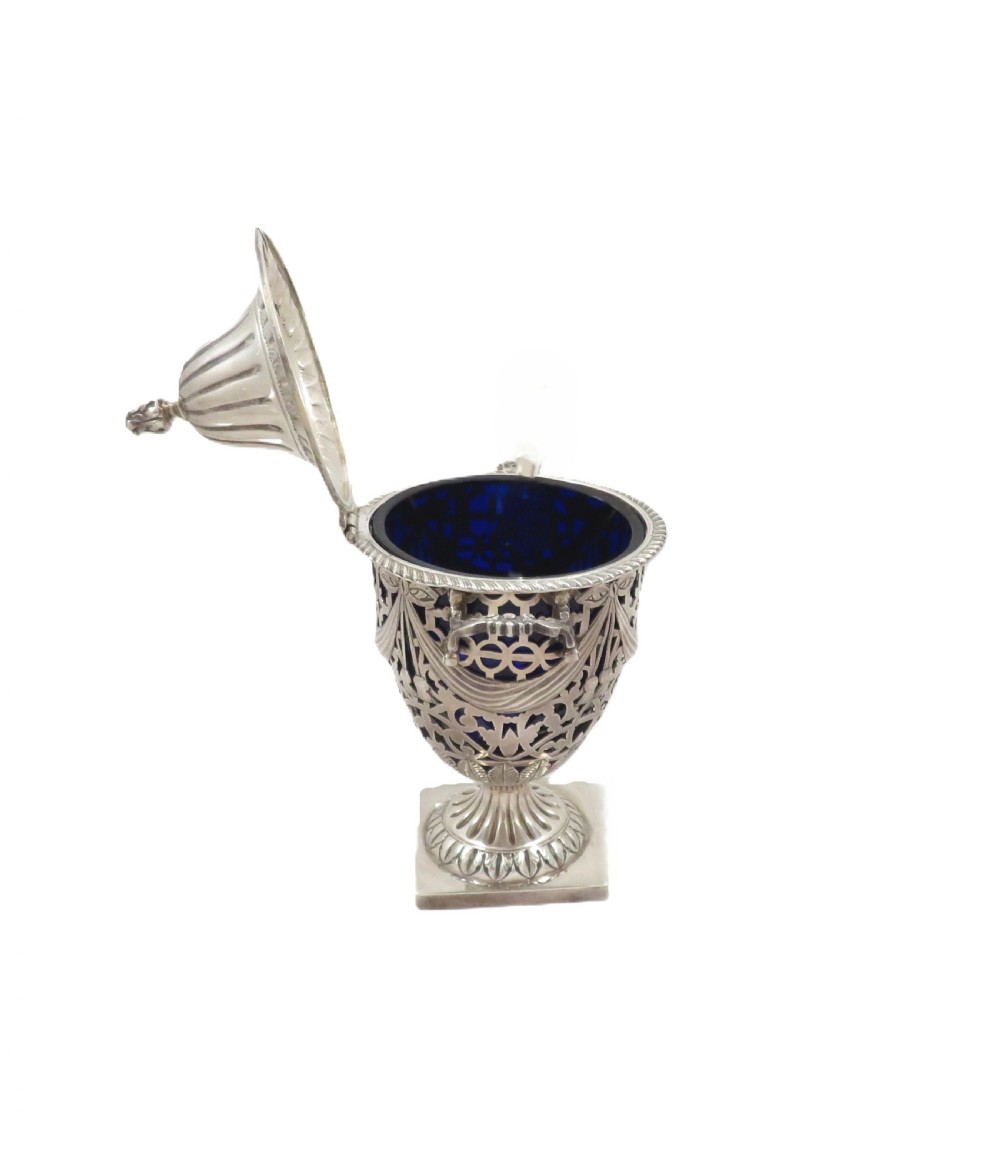 An Edwardian sterling silver sugar urn featuring pierced garland decoration, a cobalt blue glass liner, a fluted lid, and a silver spoon. View VII