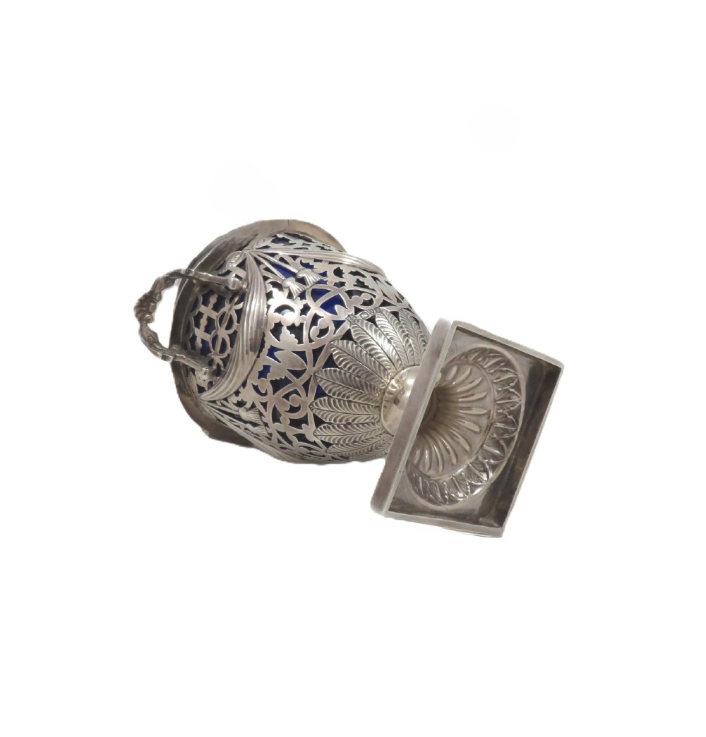 An Edwardian sterling silver sugar urn featuring pierced garland decoration, a cobalt blue glass liner, a fluted lid, and a silver spoon. View VIII