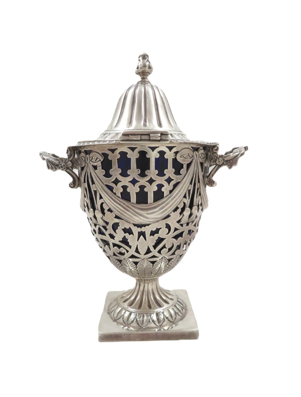 An Edwardian sterling silver sugar urn featuring pierced garland decoration, a cobalt blue glass liner, a fluted lid, and a silver spoon. View IX