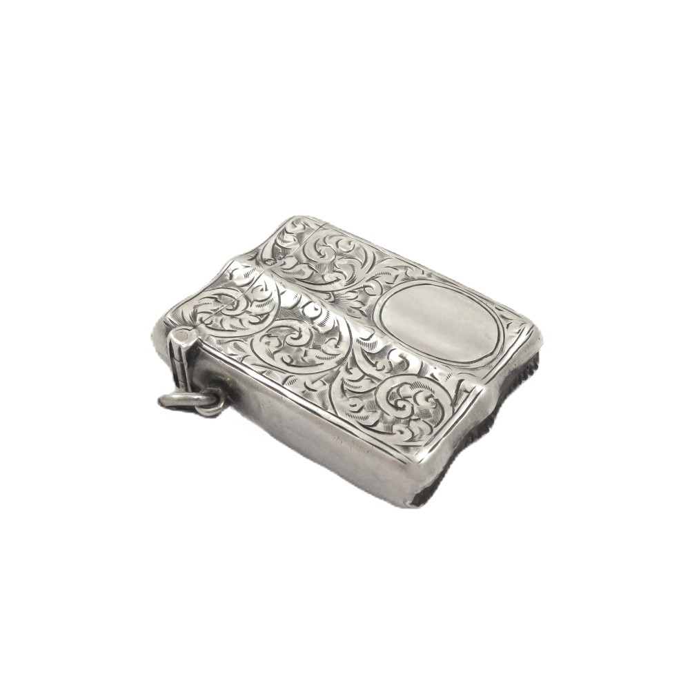 A shaped sterling silver vesta case featuring detailed scrollwork floral engraving, a vacant oval cartouche, and a side suspension ring.