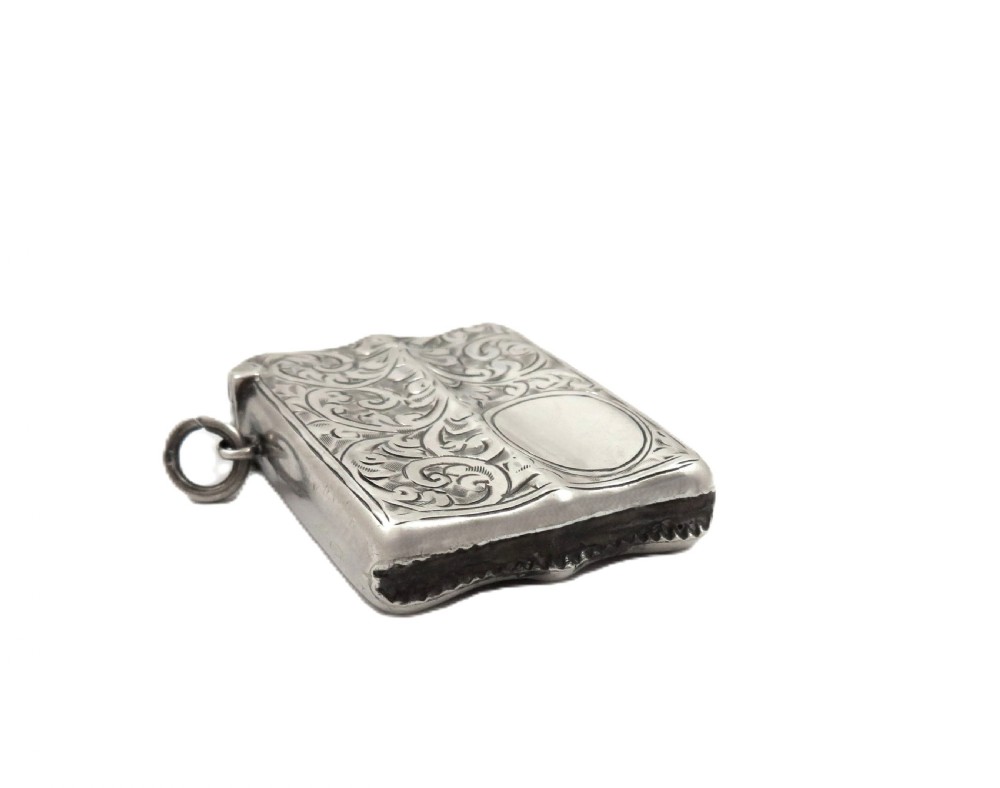 A shaped sterling silver vesta case featuring detailed scrollwork floral engraving, a vacant oval cartouche, and a side suspension ring. View V