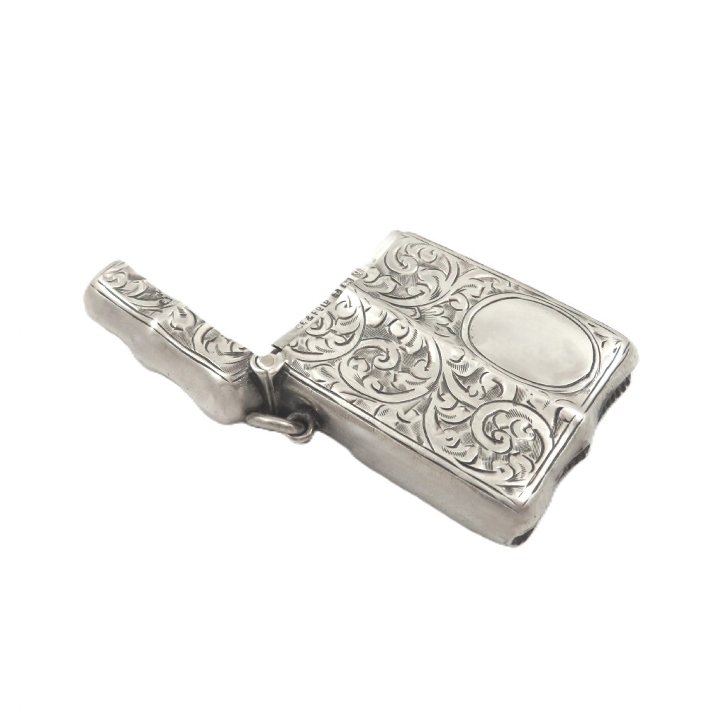 A shaped sterling silver vesta case featuring detailed scrollwork floral engraving, a vacant oval cartouche, and a side suspension ring. View VI