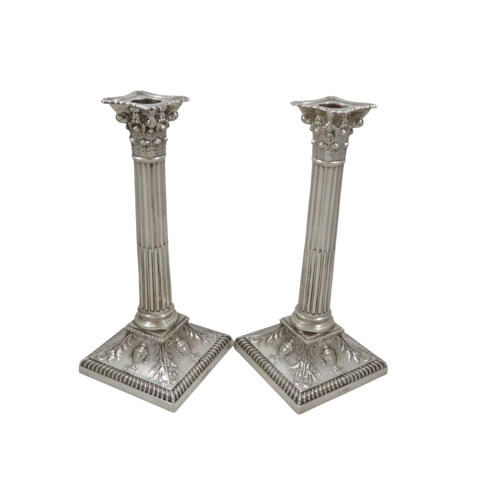 A pair of sterling silver candlesticks featuring fluted Corinthian columns mounted on square bases with urn and acanthus leaf decoration.