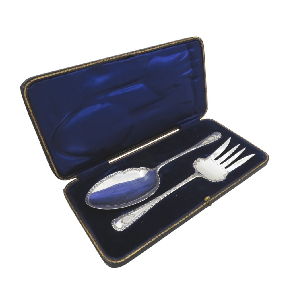 An opened dark case with cobalt blue lining displaying a pair of Edwardian sterling silver serving utensils.