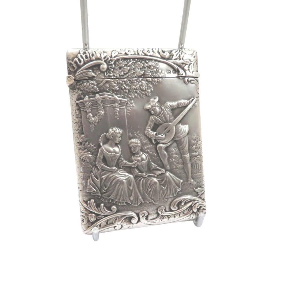 An Edwardian sterling silver card case featuring an embossed relief scene of figures playing music outdoors.