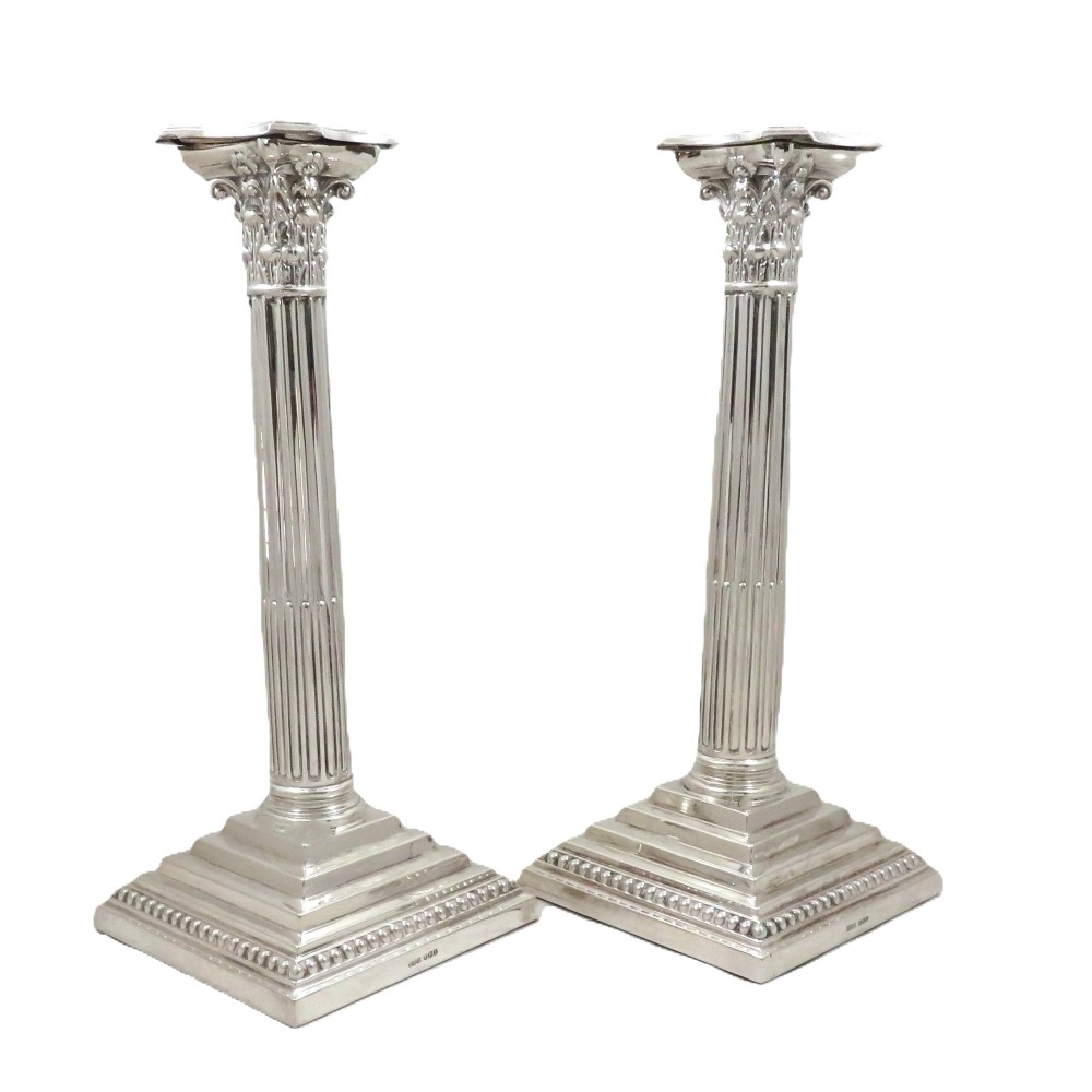 A pair of hallmarked sterling silver candlesticks featuring fluted Corinthian columns and square stepped bases with beaded trim.