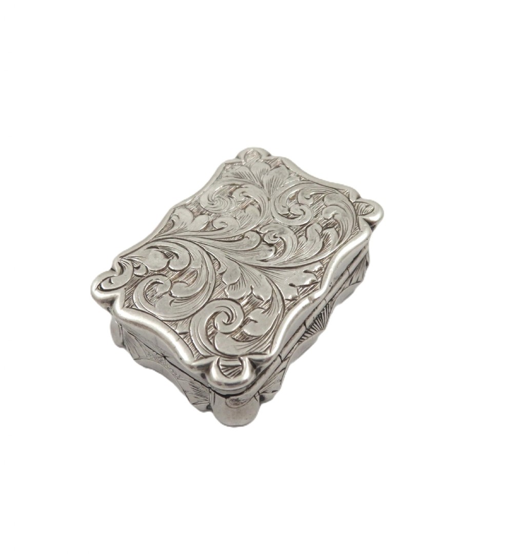 A small rectangular Victorian sterling silver vinaigrette box featuring intricate foliate engraving and a serpentine outline. View IV