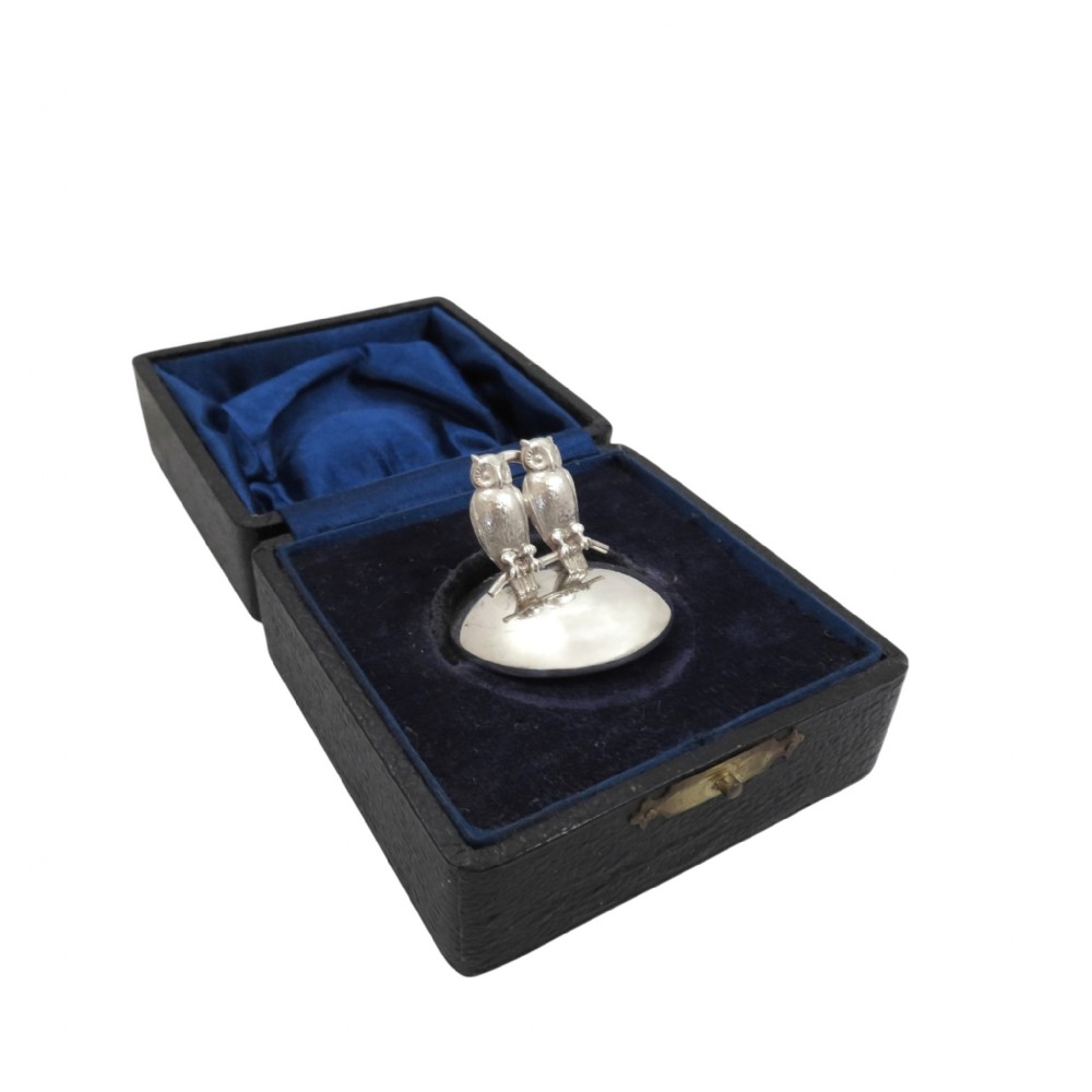 An antique sterling silver menu holder featuring two owls perched on a branch atop a circular silver base inside a navy blue velvet-lined box.