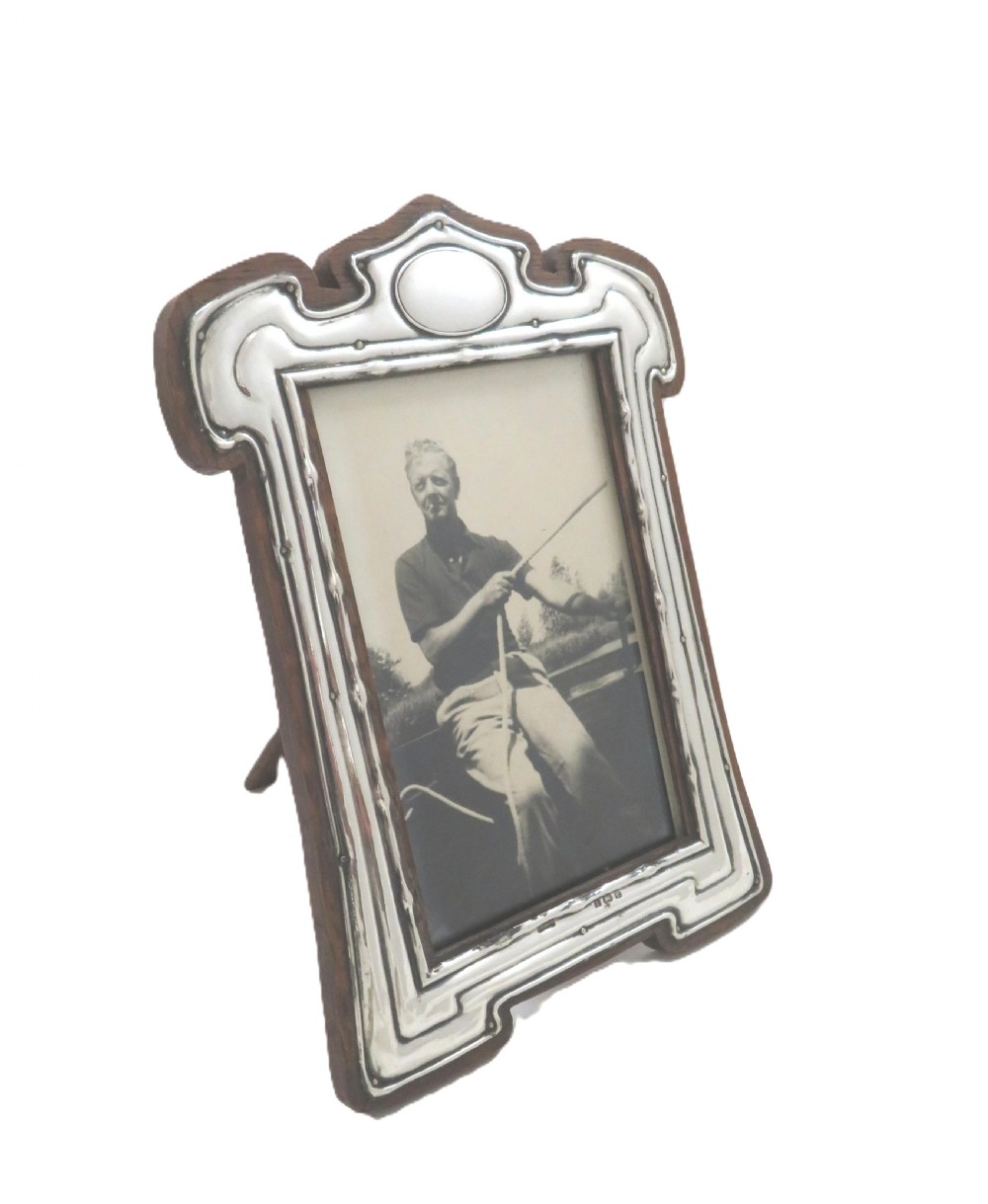 An Art Nouveau sterling silver photo frame with fluid curves mounted on a dark wooden backing. View V