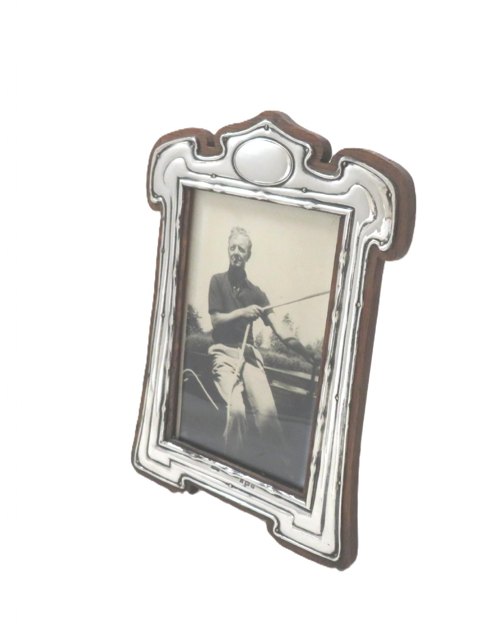 An Art Nouveau sterling silver photo frame with fluid curves mounted on a dark wooden backing. View VII