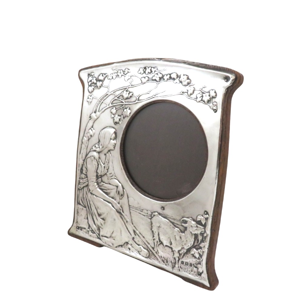An Art Nouveau sterling silver photo frame featuring an embossed scene of a seated girl beneath a tree with a goat beside a circular opening. View VI