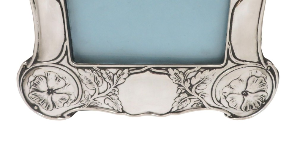 An upright sterling silver picture frame decorated with embossed Art Nouveau floral motifs and sinuous curves around an arched rectangular aperture. View VI