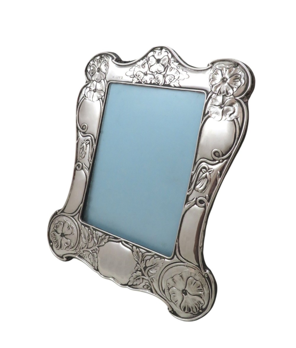 An upright sterling silver picture frame decorated with embossed Art Nouveau floral motifs and sinuous curves around an arched rectangular aperture. View VII