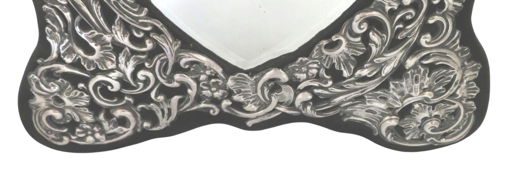 An Edwardian sterling silver dressing table mirror featuring elaborate repousse scrollwork detailing and an easel backing. View VI