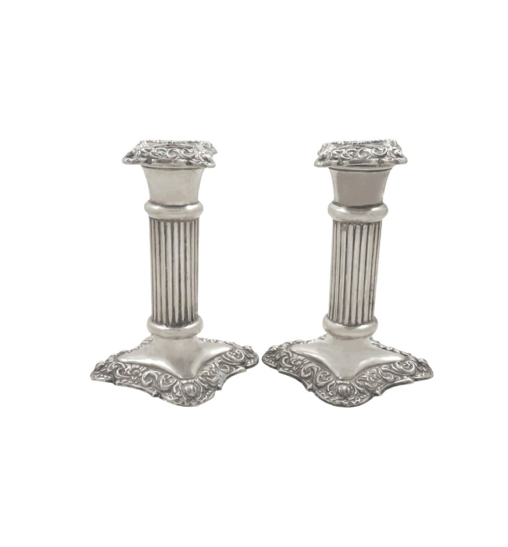 A pair of Edwardian sterling silver candlesticks featuring fluted columns and embossed ornate scrollwork bases. View V