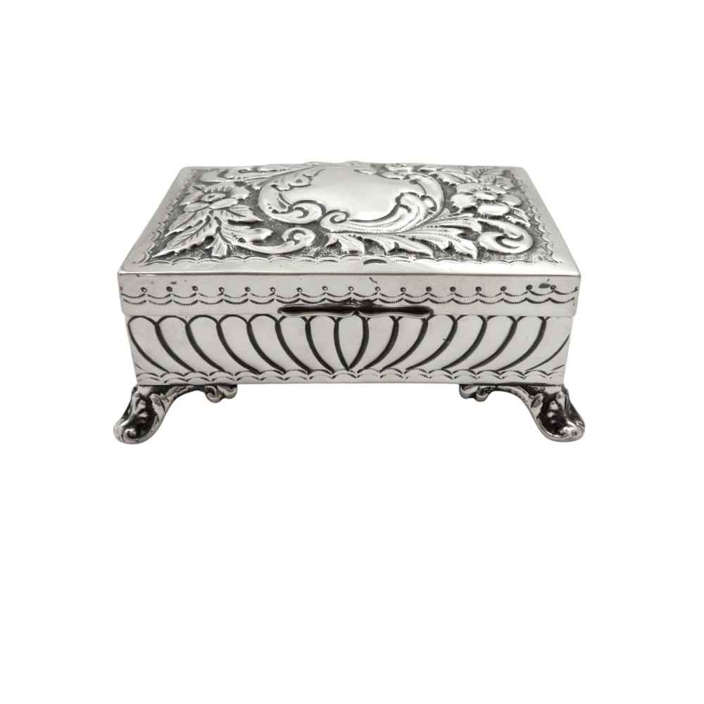 An Edwardian sterling silver rectangular trinket box featuring floral repousse scrollwork on the hinged lid, fluted sides, and small cast feet.