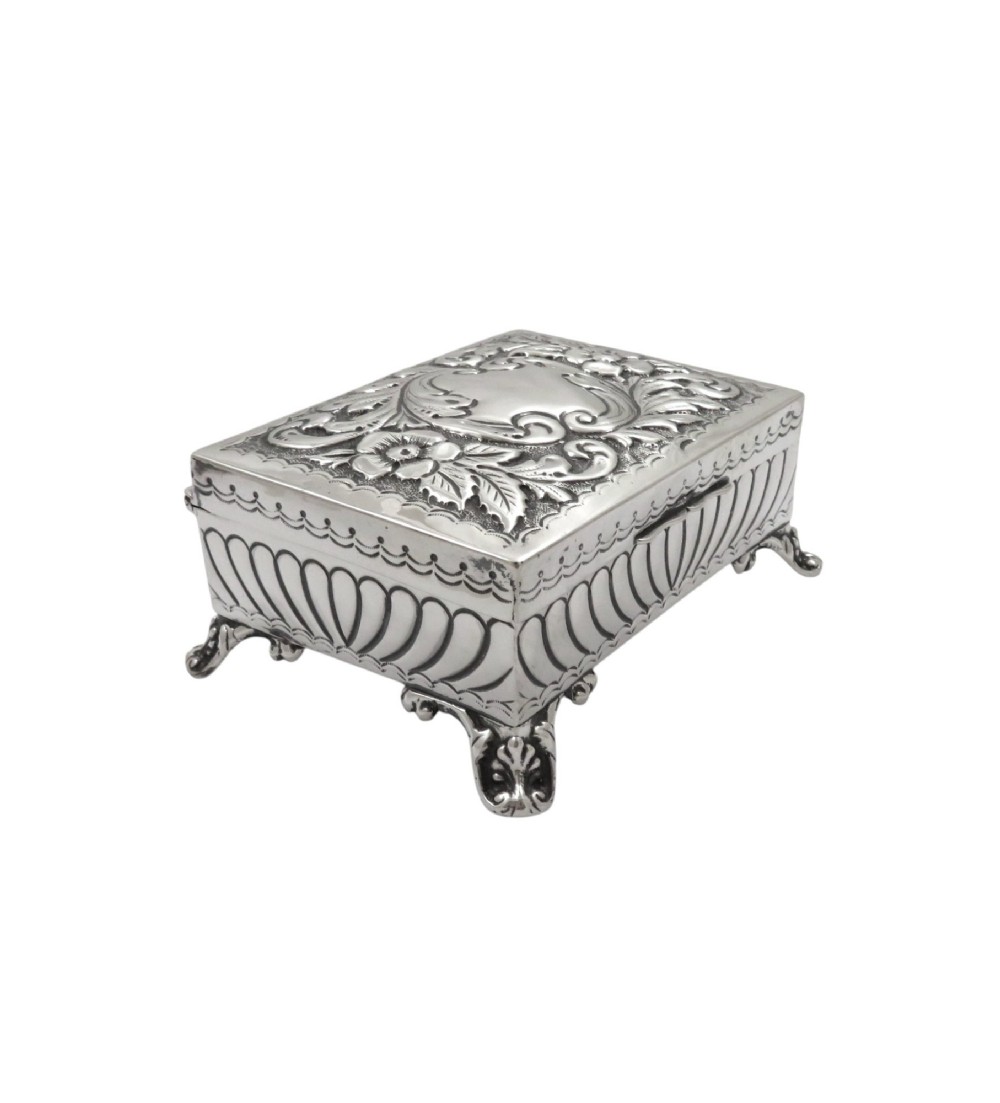 An Edwardian sterling silver rectangular trinket box featuring floral repousse scrollwork on the hinged lid, fluted sides, and small cast feet. View IV