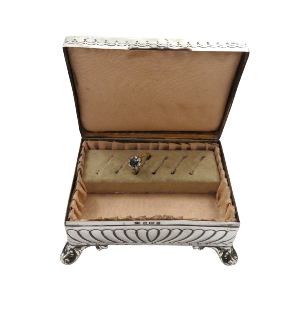 An Edwardian sterling silver rectangular trinket box featuring floral repousse scrollwork on the hinged lid, fluted sides, and small cast feet. View V