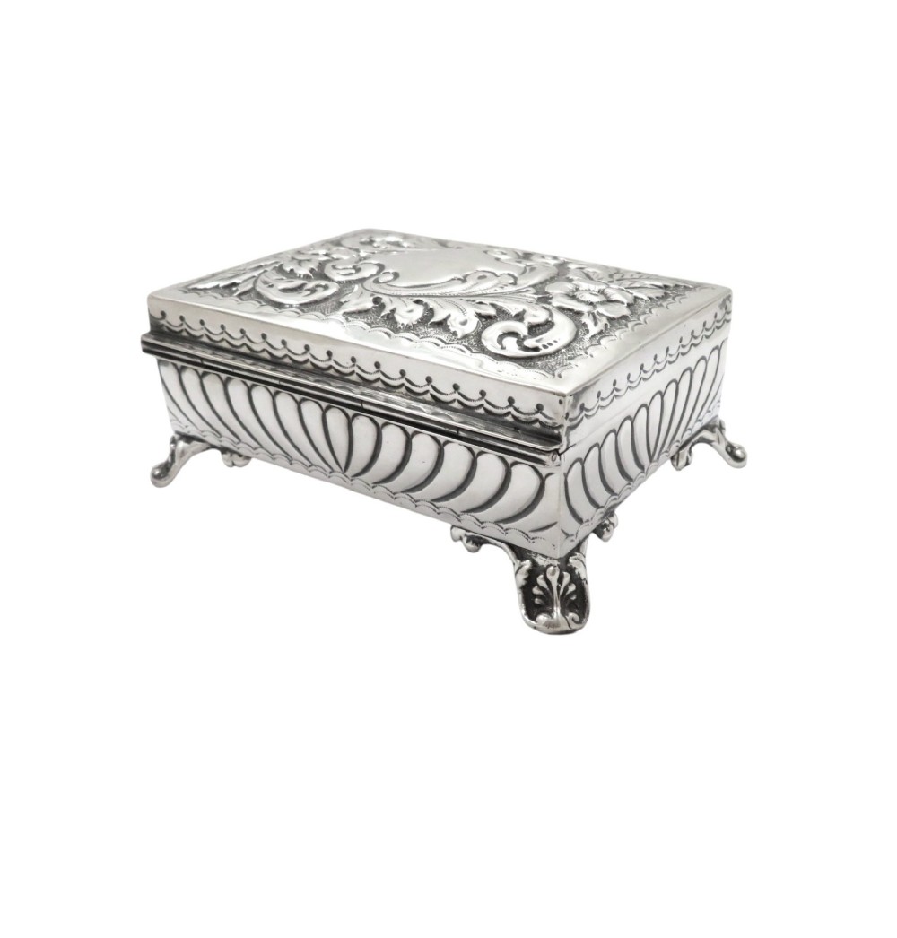 An Edwardian sterling silver rectangular trinket box featuring floral repousse scrollwork on the hinged lid, fluted sides, and small cast feet. View VI