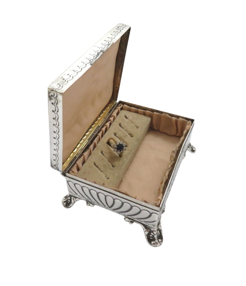 An Edwardian sterling silver rectangular trinket box featuring floral repousse scrollwork on the hinged lid, fluted sides, and small cast feet. View VII