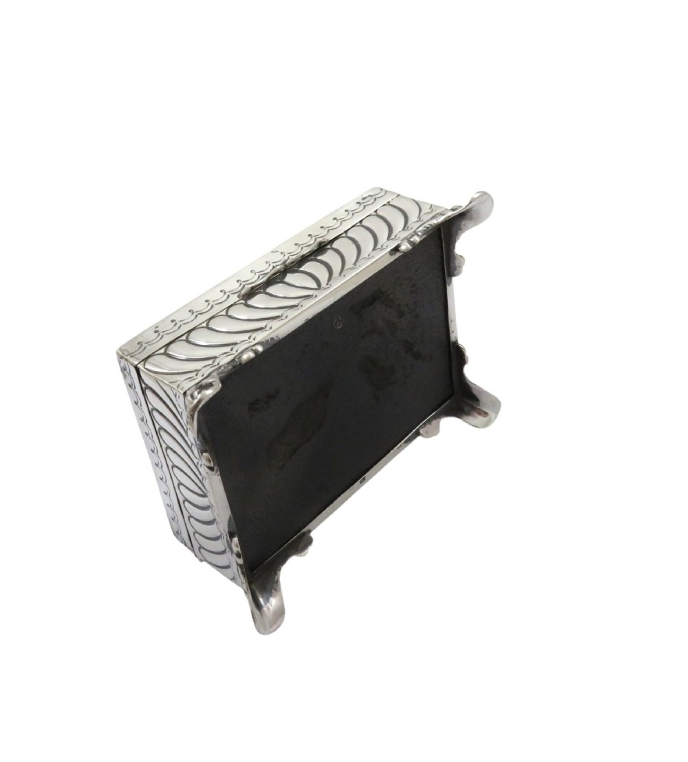 An Edwardian sterling silver rectangular trinket box featuring floral repousse scrollwork on the hinged lid, fluted sides, and small cast feet. View IX