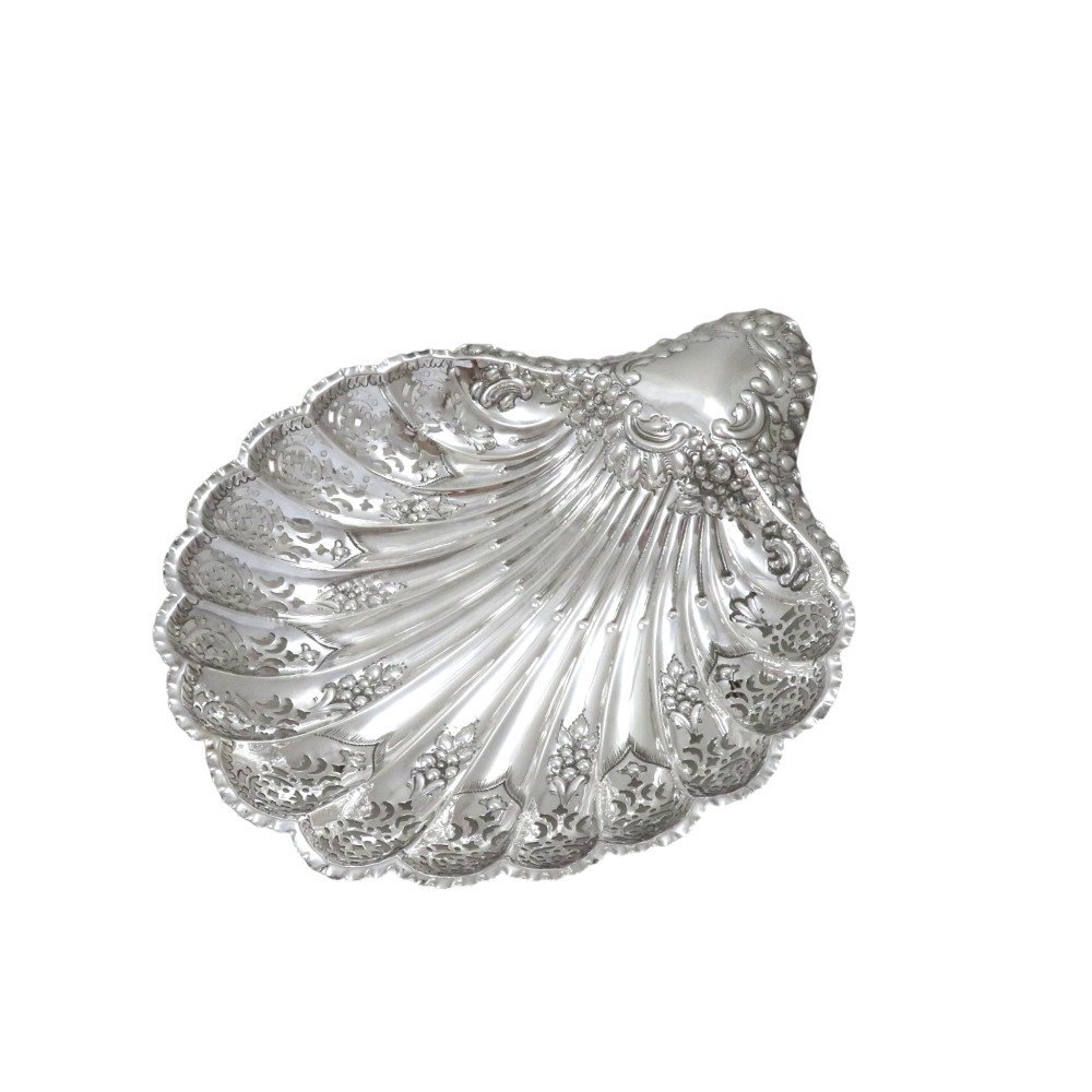 A Victorian sterling silver dish shaped like a scallop shell with intricate repousse foliage and pierced fluted details.