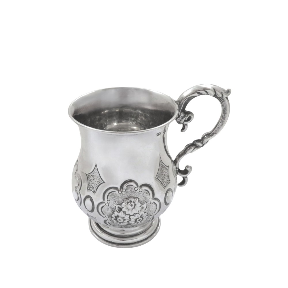 A Victorian sterling silver christening mug featuring floral chasing, geometric embossing, and a scroll handle.