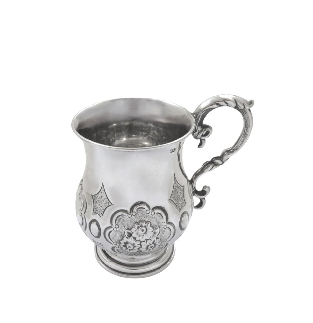 A Victorian sterling silver christening mug featuring floral chasing, geometric embossing, and a scroll handle. View VI