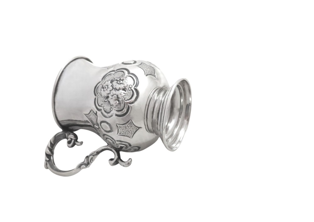 A Victorian sterling silver christening mug featuring floral chasing, geometric embossing, and a scroll handle. View VIII