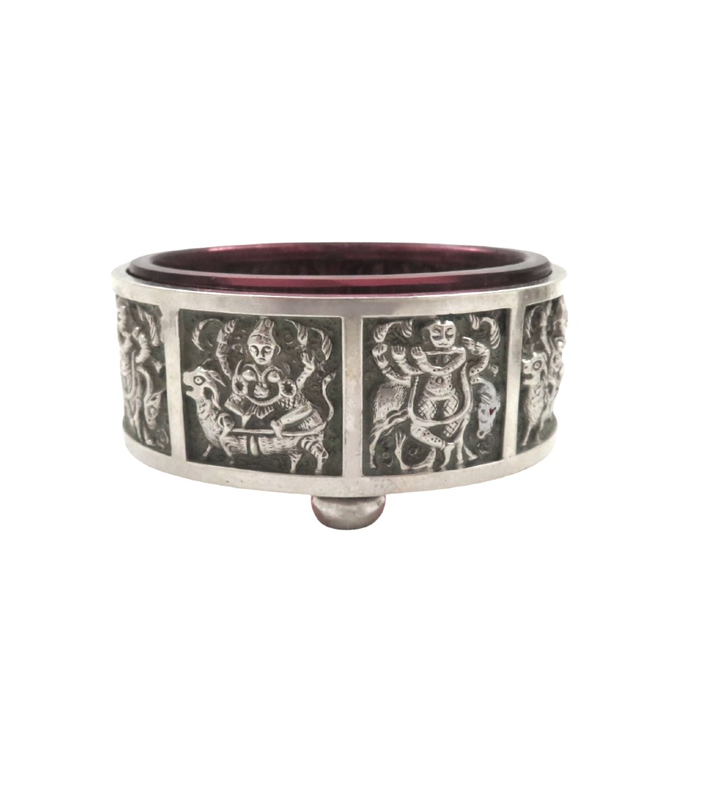 A pair of circular sterling silver salt cellars with red glass liners and matching spoons featuring Hindu deity relief panels, housed inside a velvet-lined presentation case. View IV