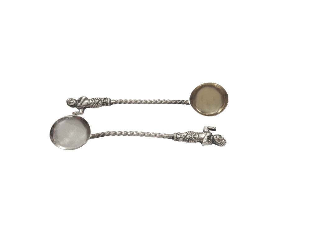 A pair of circular sterling silver salt cellars with red glass liners and matching spoons featuring Hindu deity relief panels, housed inside a velvet-lined presentation case. View V