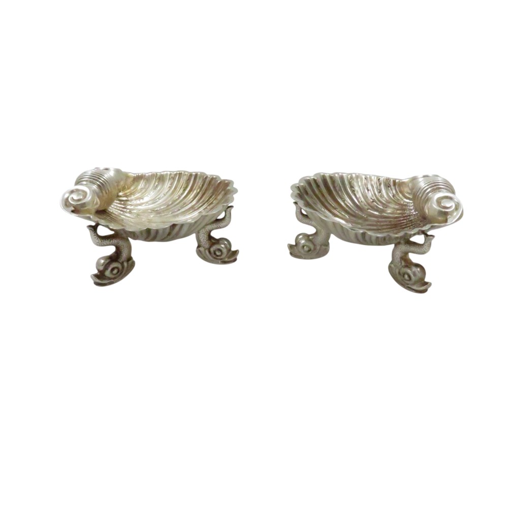 A pair of Victorian sterling silver open salt cellars shaped like scallop shells supported by cast dolphin feet.