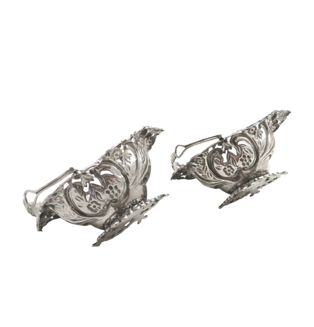 A pair of Edwardian sterling silver baskets featuring pierced floral openwork, swing handles, and scroll feet. View V