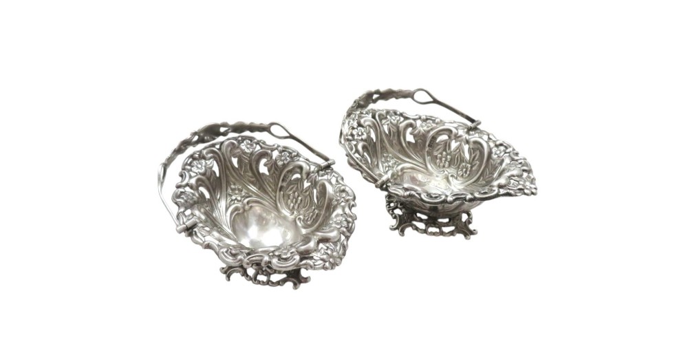 A pair of Edwardian sterling silver baskets featuring pierced floral openwork, swing handles, and scroll feet. View VII