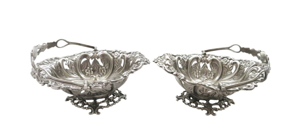 A pair of Edwardian sterling silver baskets featuring pierced floral openwork, swing handles, and scroll feet. View IX