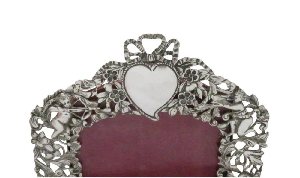 An ornate late Victorian sterling silver easel-back photo frame decorated with pierced cherubs, birds, and floral scrollwork, fitted with a burgundy velvet backing. View IV