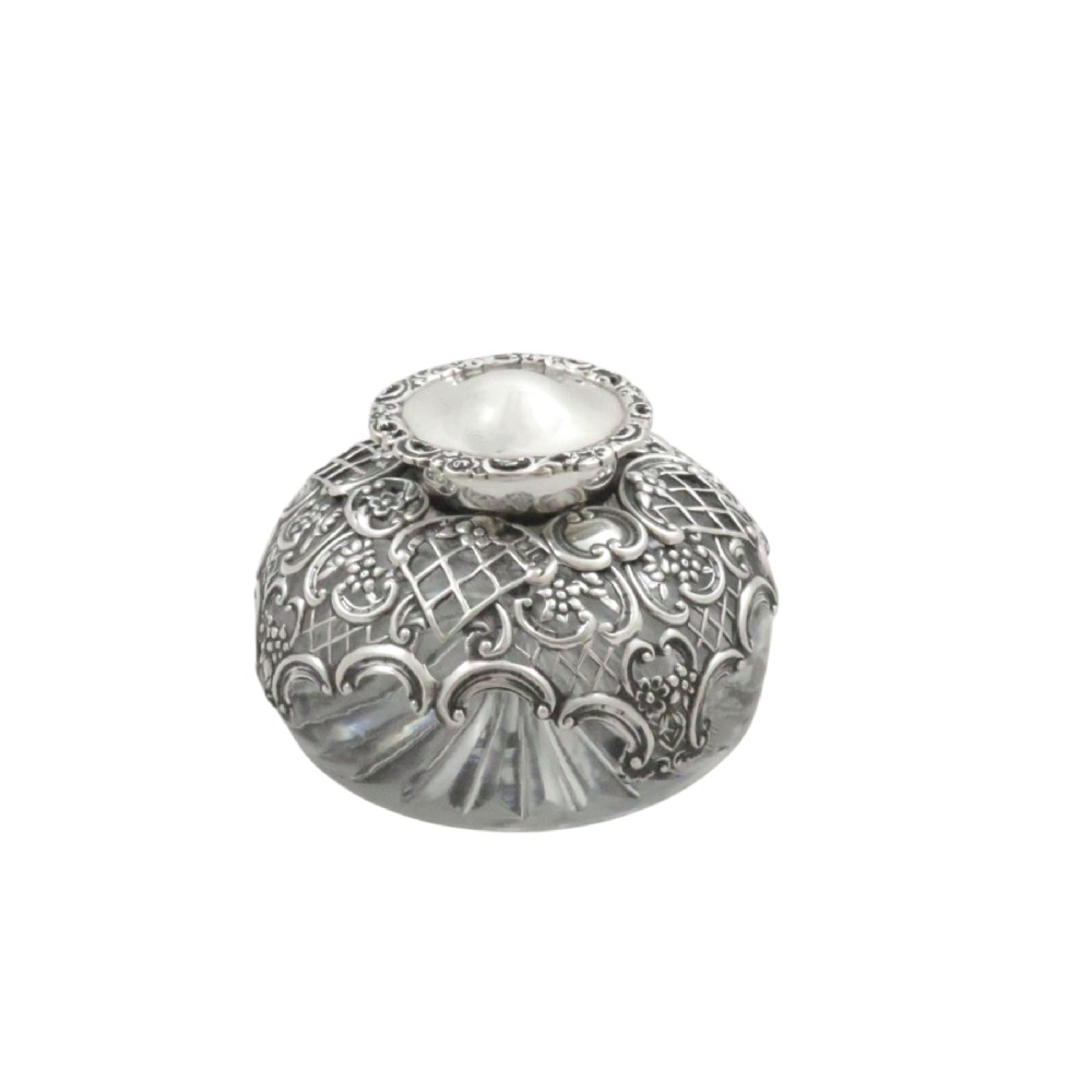 An antique Victorian clear cut-glass inkwell featuring an intricate repousse sterling silver collar and hinged lid.