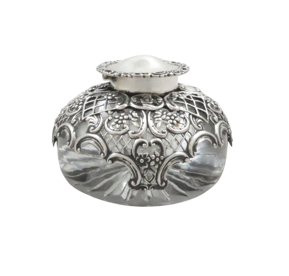 An antique Victorian clear cut-glass inkwell featuring an intricate repousse sterling silver collar and hinged lid. View IV