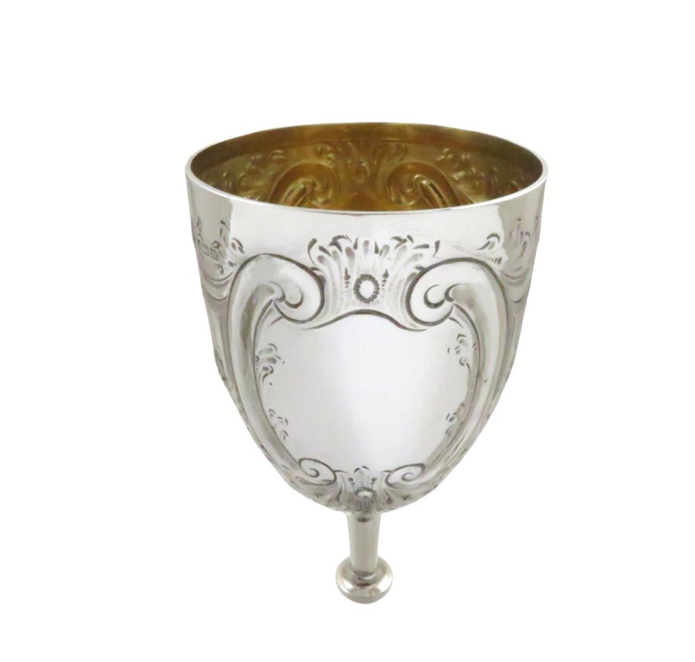 An Edwardian sterling silver wine goblet featuring scroll repousse engraving, an unengraved central cartouche, a knopped stem, and a gilt interior. View VII