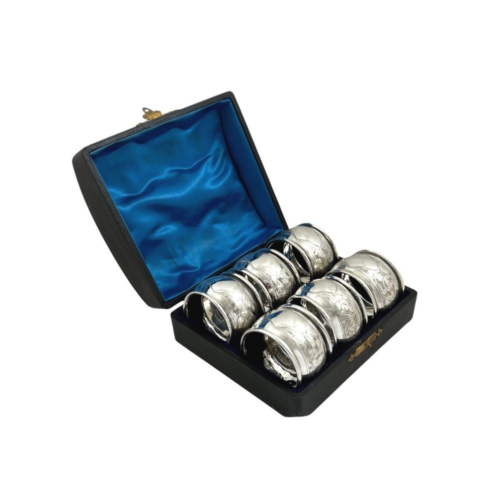 A set of six engraved sterling silver napkin rings arranged inside a black fitted presentation case lined with bright blue silk.