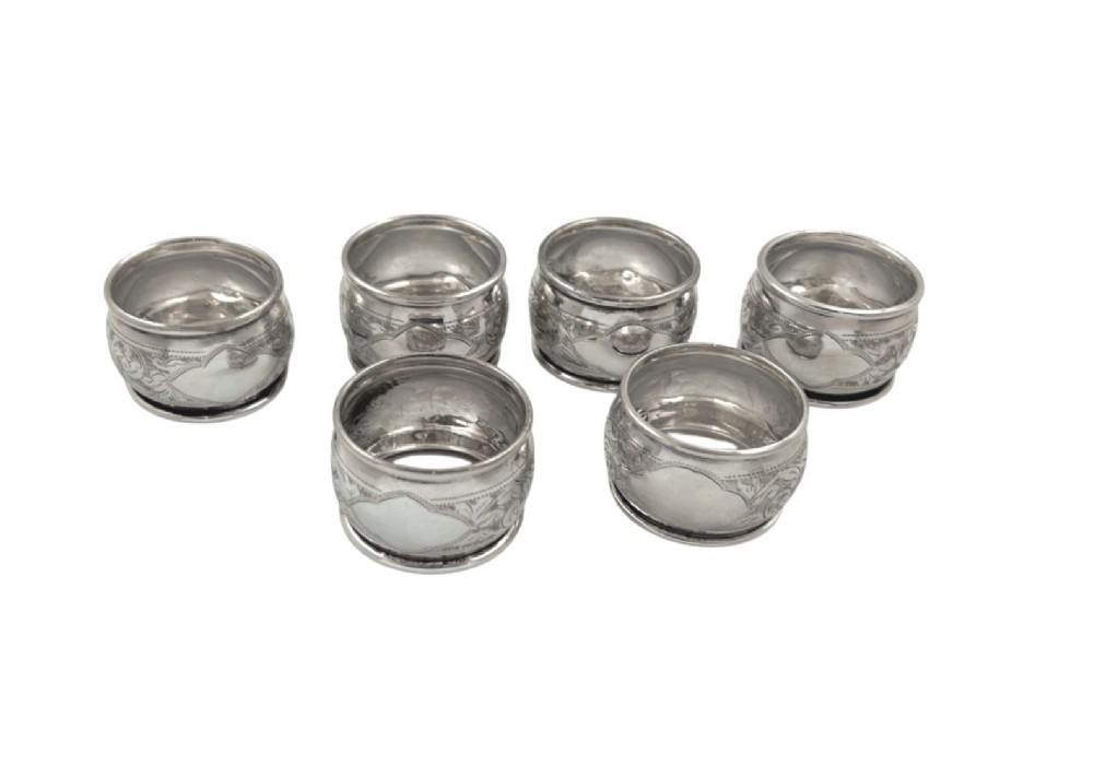 A set of six engraved sterling silver napkin rings arranged inside a black fitted presentation case lined with bright blue silk. View III