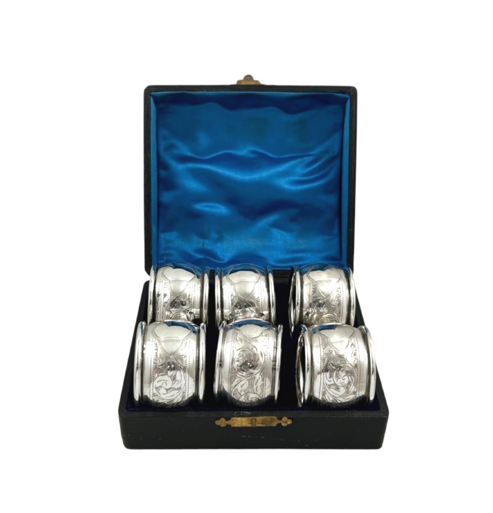 A set of six engraved sterling silver napkin rings arranged inside a black fitted presentation case lined with bright blue silk. View VII