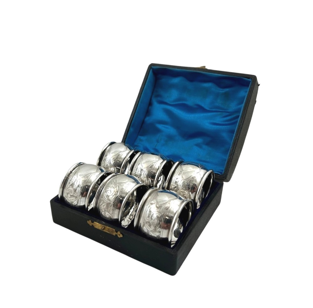 A set of six engraved sterling silver napkin rings arranged inside a black fitted presentation case lined with bright blue silk. View IX